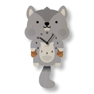 May include: A gray wooden squirrel-shaped wall clock with black clock hands and a white clock face. The clock has a tail and holds two brown acorns. The clock face has the text "popclox".