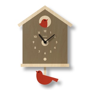 May include: A wooden cuckoo clock in the shape of a birdhouse. The clock face is brown with black hands and white numbers. A red bird is in a circular window and another red bird hangs below. The clock has the word "popclox" printed on the face.