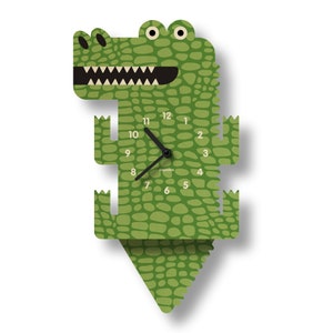 May include: A green alligator-shaped wall clock with a textured pattern. The clock features black hands, white teeth, and a black mouth. The clock face displays numbers 1 through 12. The clock is approximately 20 inches tall.