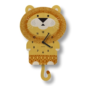 May include: A wooden lion-shaped wall clock with a yellow and brown color scheme. The clock features a lion's face with a textured mane, a black nose, and black clock hands. The clock face has black numbers and the brand name "popclox".