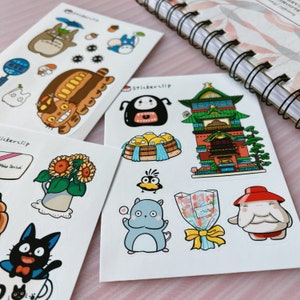 May include: A set of three sticker sheets featuring characters and scenes from the animated film Spirited Away. The stickers are printed on white paper and have a glossy finish. The first sheet features Totoro, the No Face spirit, and a bus. The second sheet features a sunflower, a black cat, and a teacup. The third sheet features a No Face spirit, a building, a bird, a cat, a bouquet of flowers, and a character with a red hat.