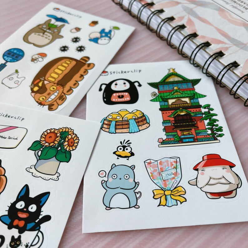 May include: A set of three sticker sheets featuring characters and scenes from the animated film Spirited Away. The stickers are printed on white paper and have a glossy finish. The first sheet features Totoro, the No Face spirit, and a bus. The second sheet features a sunflower, a black cat, and a teacup. The third sheet features a No Face spirit, a building, a bird, a cat, a bouquet of flowers, and a character with a red hat.