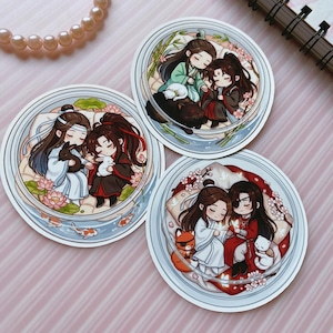May include: Three circular stickers featuring chibi-style anime characters resting together. Each sticker depicts two figures in traditional robes surrounded by elements like lotus flowers, bamboo, koi fish, small animals, and cherry blossoms in soft colors.