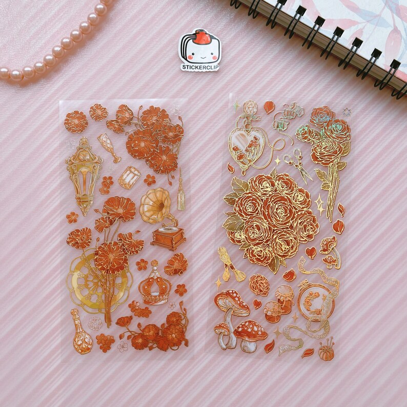 May include: Two sheets of clear sticker paper with gold foil accents. The stickers feature floral designs, a gramophone, a bottle, a crown, and a lantern. The stickers are perfect for adding a touch of elegance to journals, planners, and other craft projects.