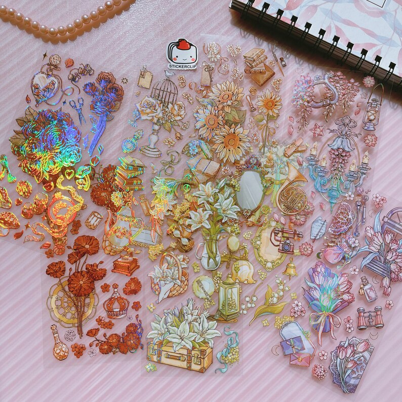 May include: A sheet of iridescent holographic stickers featuring a variety of designs, including flowers, books, musical instruments, and other whimsical elements. The stickers are perfect for adding a touch of sparkle and magic to journals, planners, and other craft projects.