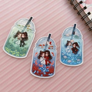 May include: Three die-cut stickers shaped like bubble tea cups, each containing two chibi-style characters. The left is green with plants, the centre is orange with coral and fish, and the right is blue with lotus flowers and a small black rabbit.