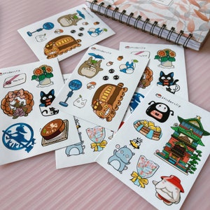 May include: A set of 10 sticker sheets featuring characters from the Studio Ghibli films, including Totoro, Kiki's Delivery Service, and Spirited Away. The stickers are printed on white paper and have a glossy finish. The sticker sheets are packaged in clear plastic sleeves.