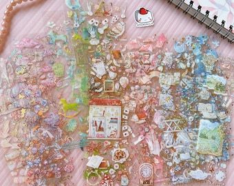 May include: A sheet of clear, transparent stickers with a variety of whimsical designs. The stickers feature a mix of pastel colors, gold accents, and illustrations of flowers, butterflies, stars, and other magical elements. The sheet also includes a sticker of a small shop with the words "The Magic" written on it.