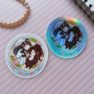 May include: Two circular stickers featuring a chibi-style illustration of two figures with long dark hair, one in white and blue robes and one in black and red robes, each holding a small rabbit, surrounded by lotus flowers and koi fish.
