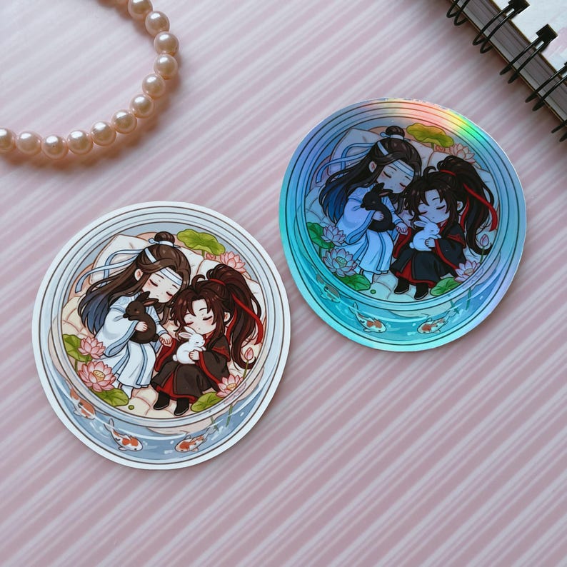 May include: Two circular stickers featuring a chibi-style illustration of two figures with long dark hair, one in white and blue robes and one in black and red robes, each holding a small rabbit, surrounded by lotus flowers and koi fish.