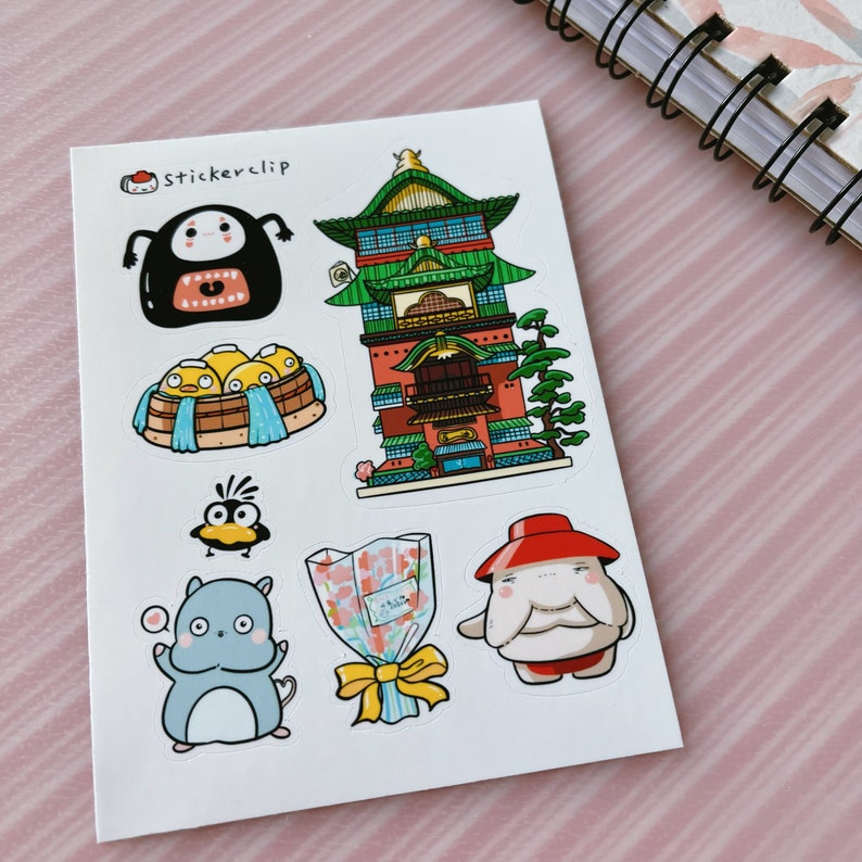 May include: A sheet of stickers featuring various characters and objects from the animated film Spirited Away. The stickers include a red and green building, a bathhouse with yellow ducklings, a black and white creature with a mouth, a blue creature with a heart, a bird, a bouquet of flowers, and a white creature with a red hat.