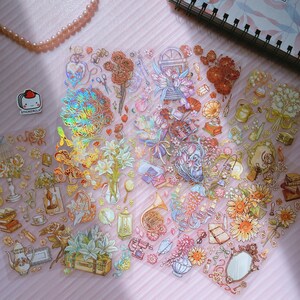 May include: A sheet of iridescent stickers featuring a variety of floral designs, including roses, lilies, and sunflowers. There are also several other decorative elements, such as a vintage suitcase, a musical instrument, and a mirror.