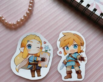 May include: Two die-cut stickers featuring cartoon characters. One shows a blonde character holding a gift box with a blue flower, and the other depicts a character with a sword. Both have large eyes and are surrounded by hearts.