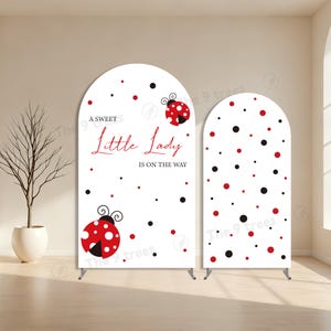 May include: Two white arched backdrop banners with ladybug and polka dot designs. One banner has the text "A Sweet Little Lady Is On The Way" in red script. The other banner has a polka dot pattern.