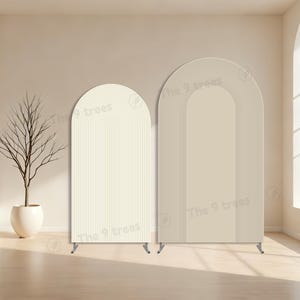 Op de afbeelding: Twee gebogen decoratieve panelen in crème- en beigetinten. Het linkerpaneel heeft verticale lijnen, het rechterpaneel concentrische booglijnen. Beide hebben kleine metalen voetjes. In een kamer met een neutraal kleurenpalet.