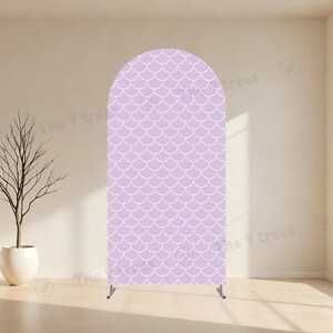 May include: An arched backdrop stand featuring a light purple fabric cover with a repeating white fish scale pattern. The structure is supported by a thin metal frame at the base, displaying the text The 9 trees faintly across the surface.