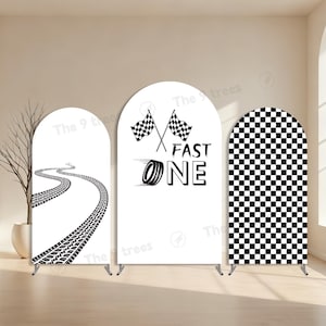 May include: Three white arched backdrop displays with racing themes. One features a tire track design, another has crossed checkered flags and the words "FAST ONE", and the third has a checkered pattern.