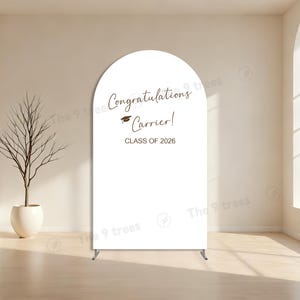 Puede incluir: Arco de graduación blanco con el texto "¡Felicidades Carrier!" y "CLASE DE 2026". El arco está sostenido por un soporte metálico, perfecto para celebraciones de graduación.