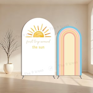 Puede incluir: Dos soportes de fondo arqueados. Uno presenta un sol en acuarela con el texto "first trip around the sun". El otro tiene un diseño de arcoíris en colores pastel. Ambos están sobre soportes metálicos.