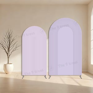 Op de afbeelding: Twee boogvormige, lavendelkleurige achtergrondpanelen met verticale en gebogen lijnen. De panelen hebben een minimalistisch ontwerp en worden ondersteund door kleine metalen poten. De tekst "The 9 trees" is zichtbaar op de panelen.