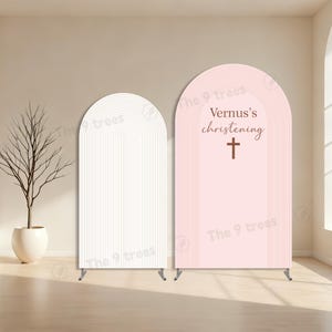 Puede incluir: Dos soportes de fondo arqueados. Uno es blanco con líneas verticales, el otro es rosa con el texto "Vernus's christening" y una cruz. Ambos tienen soportes metálicos y son para eventos.