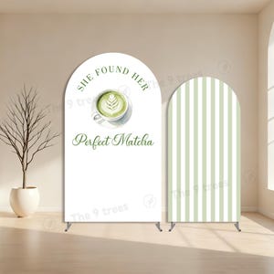 Könnte beinhalten: Zwei weiße, bogenförmige Backdrop-Displays. Eines zeigt den Text "She Found Her Perfect Matcha" mit einer Matcha-Latte-Illustration. Das andere hat vertikale grüne und weiße Streifen. Beide haben Metallständer.