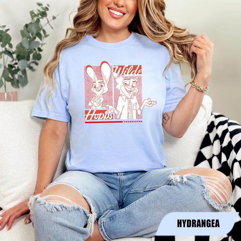 Puede incluir: Camiseta azul claro con un gr&aacute;fico rojo de dos personajes de dibujos animados, un conejo y un zorro, con el texto "Wilde Hopps Undercover". La camiseta es de un material suave.