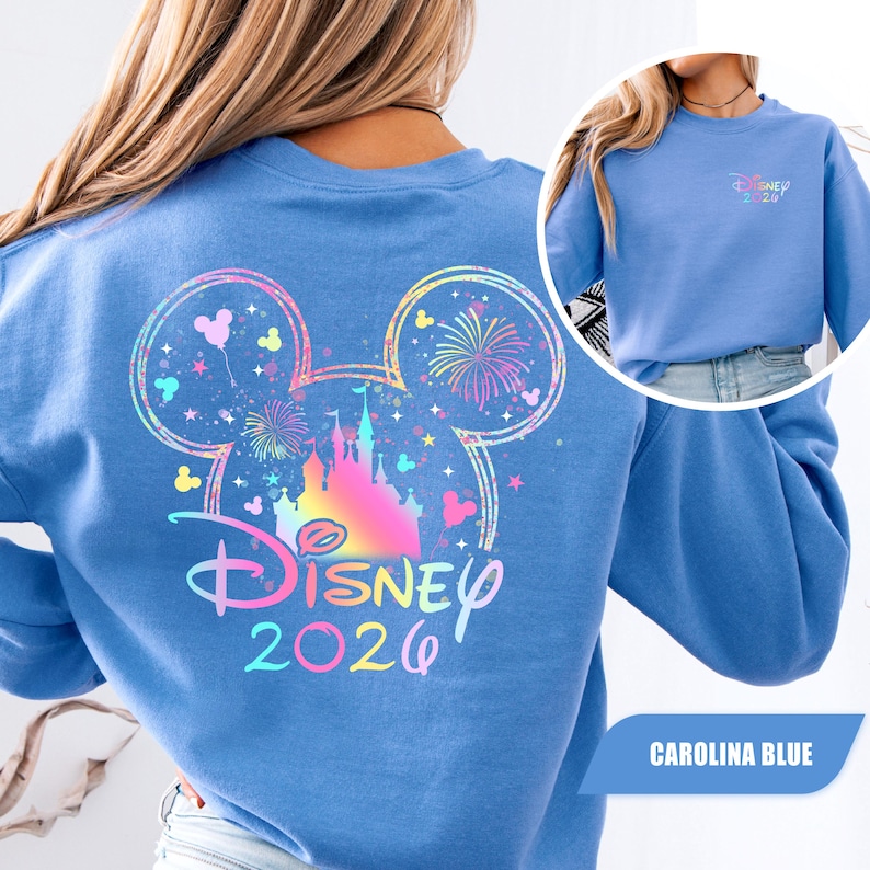 Puede incluir: Sudadera azul Carolina con un dise&ntilde;o colorido de Disney. La parte trasera muestra una gran cabeza de Mickey Mouse con un castillo, fuegos artificiales y el texto "Disney 2026". Una versi&oacute;n m&aacute;s peque&ntilde;a del dise&ntilde;o est&aacute; en el frente. Estilo casual y c&oacute;modo.