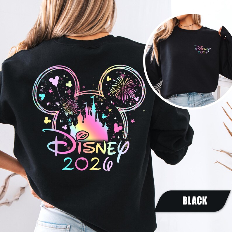 Puede incluir: Sudadera negra con un dise&ntilde;o colorido de Disney con el texto "Disney 2026". El dise&ntilde;o incluye fuegos artificiales, un castillo y orejas de Mickey Mouse. Una versi&oacute;n m&aacute;s peque&ntilde;a del dise&ntilde;o est&aacute; en la manga.