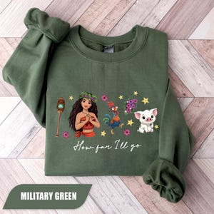 Pu&ograve; includere: Felpa verde militare con un'illustrazione a cartoni animati di una donna, un gallo e un maiale, con la scritta "How far I'll go". Il disegno comprende stelle e fiori. La felpa &egrave; di colore unito.