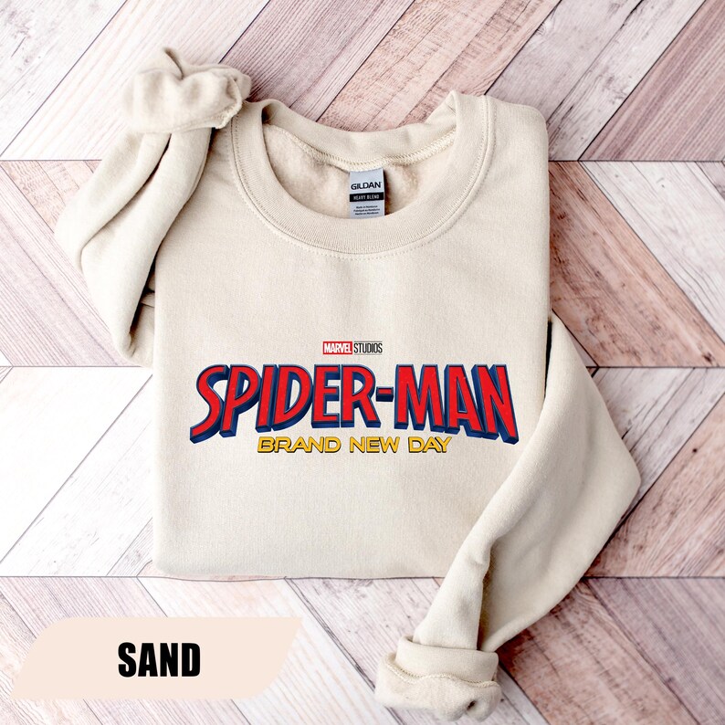 Puede incluir: Sudadera de color arena con el logotipo de Spider-Man de Marvel Studios en rojo y azul. El texto "BRAND NEW DAY" est&aacute; debajo del logotipo. La sudadera tiene cuello redondo y mangas largas.