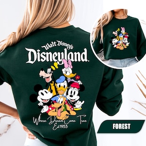 May include: A dark green crewneck sweatshirt featuring a large graphic on the back with the text Walt Disney's Disneyland Where Dreams Come True Est 1955 and illustrations of Mickey Mouse, Minnie Mouse, Donald Duck, Daisy Duck, Goofy, and Pluto.