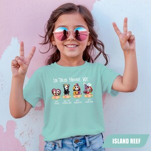 May include: A light blue t-shirt with the text "IN THIS HOUSE WE" and four cartoon characters. The shirt also has the text "LOVE FAMILY", "LOVE THE PUMPKIN KING", "LOVE HALLOWEEN", and "LOVE CHRISTMAS". The shirt is labeled "ISLAND REEF".