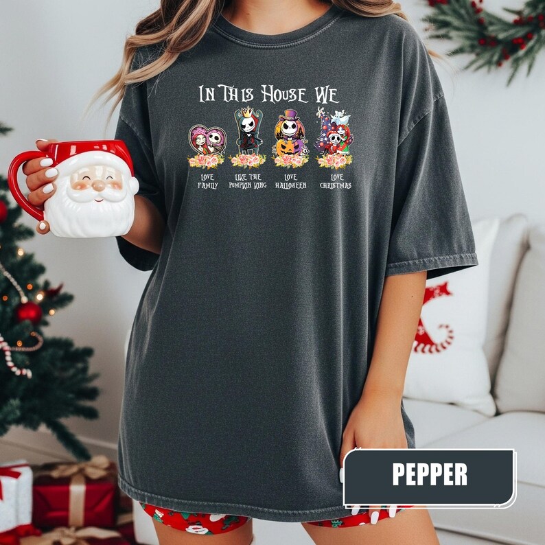 May include: A dark gray t-shirt with the text "IN THIS HOUSE WE" above four cartoon characters. Below the characters are the words "LOVE FAMILY", "LIKE THE PUMPKIN KING", "LOVE HALLOWEEN", and "LOVE CHRISTMAS". The word "PEPPER" is in a rectangle at the bottom.
