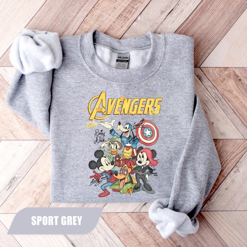 May include: A sport grey crewneck sweatshirt featuring a graphic of Disney characters dressed as Avengers. The print includes Mickey Mouse, Minnie Mouse, Goofy, Donald Duck, and Pluto with the text The Avengers and character signatures.