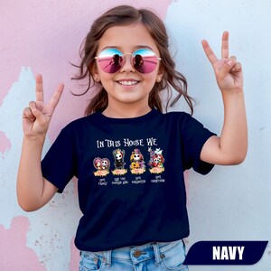 May include: Navy blue t-shirt with the text "IN THIS HOUSE WE" above cartoon characters. The shirt features the phrases "LOVE FAMILY", "LOVE PUMPKIN KING", "LOVE HALLOWEEN", and "LOVE CHRISTMAS". The word "NAVY" is at the bottom.