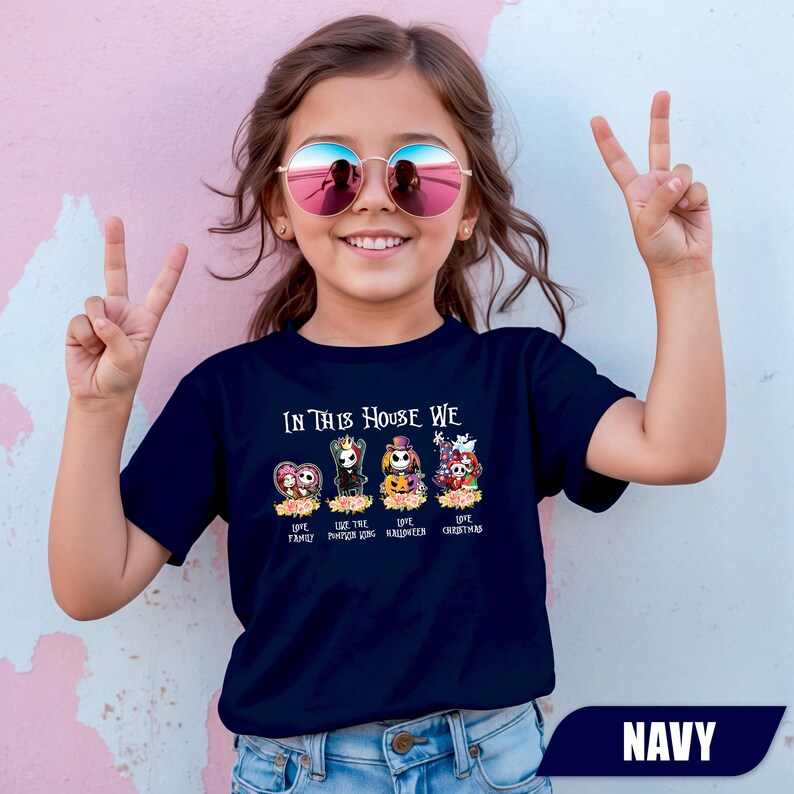 May include: Navy blue t-shirt with the text "IN THIS HOUSE WE" above cartoon characters. The shirt features the phrases "LOVE FAMILY", "LOVE PUMPKIN KING", "LOVE HALLOWEEN", and "LOVE CHRISTMAS". The word "NAVY" is at the bottom.