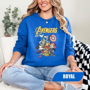 May include: A royal blue long-sleeve sweatshirt featuring a graphic print of Disney characters dressed as Avengers. The text reads The Avengers, with signatures from Mickey Mouse, Donald Duck, Goofy, and Minnie Mouse depicted in superhero costumes.