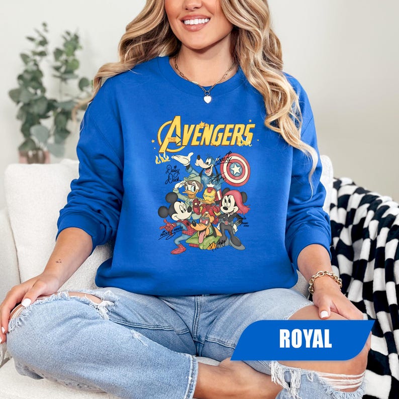 May include: A royal blue long-sleeve sweatshirt featuring a graphic print of Disney characters dressed as Avengers. The text reads The Avengers, with signatures from Mickey Mouse, Donald Duck, Goofy, and Minnie Mouse depicted in superhero costumes.