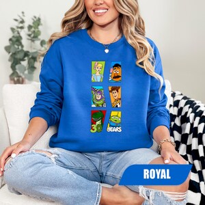 May include: A royal blue long-sleeve sweatshirt featuring a graphic print of six Toy Story characters in individual rectangular frames, including Bo Peep, Mr. Potato Head, Buzz Lightyear, Woody, Rex, and an alien, with the text 30 YEARS.