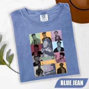 May include: A blue jean coloured t-shirt featuring a collage of photographs of a man in various poses. The centre of the graphic displays the text Still In My DONNIE Era in a mix of green, yellow, and pink lettering. The shirt has a crew neckline.
