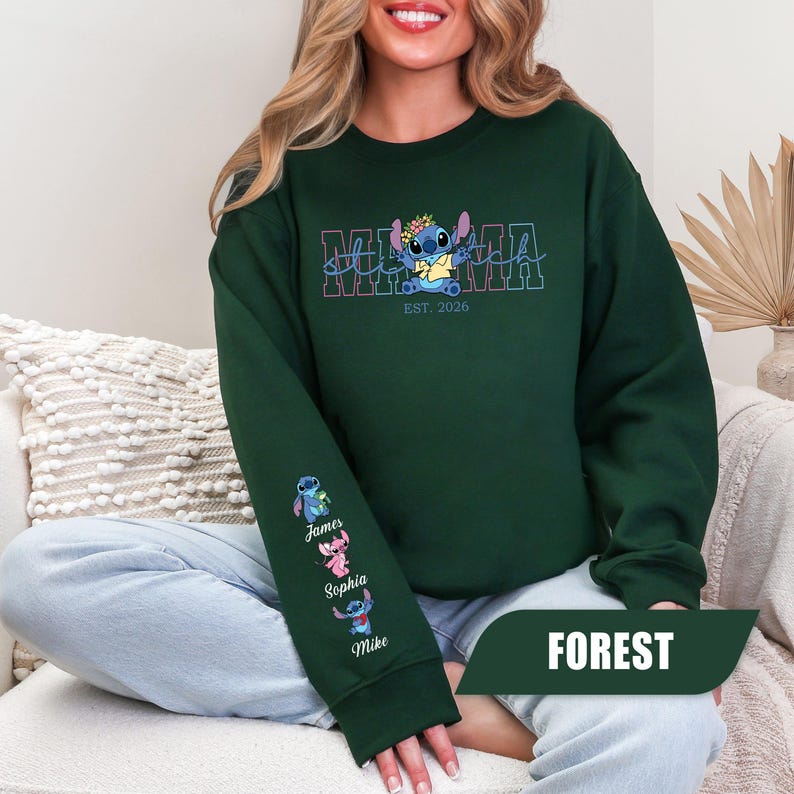 May include: A forest green crewneck sweatshirt featuring a graphic of the character Stitch wearing a flower crown above the text MAMA and EST. 2026. The left sleeve displays three small character figures with the names James, Sophia, and Mike.