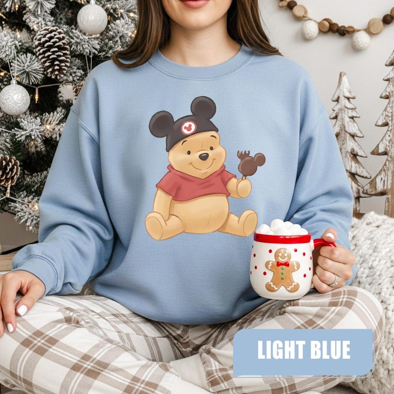 Pu&ograve; includere: Felpa azzurra con un personaggio dei cartoni animati di Winnie the Pooh con un cappello di Topolino e che tiene in mano una leccornia al cioccolato. La felpa ha un colletto rosso ed &egrave; abbinata a pantaloni a quadri. &Egrave; visibile anche una tazza di pan di zenzero.