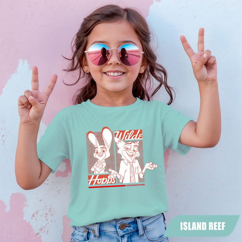 Puede incluir: Una camiseta azul claro con un gr&aacute;fico de los personajes de dibujos animados Judy Hopps y Nick Wilde. La camiseta tiene las palabras "Wilde" y "Hopps" en texto rojo. La camiseta est&aacute; etiquetada como "Island Reef".