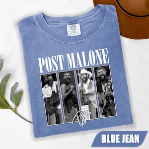 May include: Blue jean-colored t-shirt featuring the text "POST MALONE" in white block letters above a black and white image of four musicians. The shirt has a crew neck and the Comfort Colors brand label.