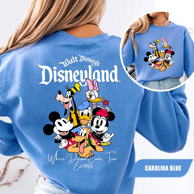 May include: A Carolina blue sweatshirt featuring a large graphic on the back with the text Walt Disney's Disneyland Where Dreams Come True Est 1955 and a group of cartoon characters including Mickey, Minnie, Donald, Daisy, Goofy, and Pluto.