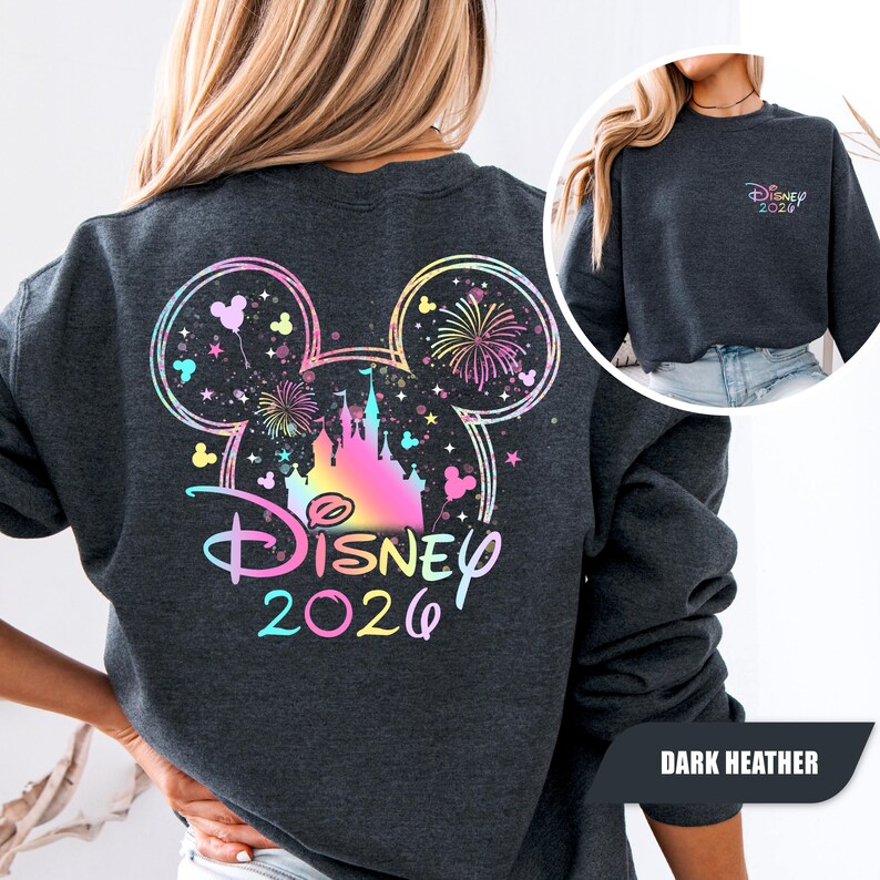 Puede incluir: Sudadera gris oscuro con un dise&ntilde;o colorido de Disney en la espalda. El dise&ntilde;o incluye un castillo, fuegos artificiales y el texto "Disney 2026" en degradado arco&iacute;ris. Una versi&oacute;n m&aacute;s peque&ntilde;a del dise&ntilde;o est&aacute; en la parte delantera.