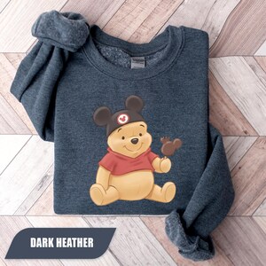 Pu&ograve; includere: Felpa color antracite scuro con un orsetto dei cartoni animati con un cappello di Topolino e un dolcetto al cioccolato. L'orso indossa una camicia rossa. Il testo "DARK HEATHER" &egrave; visualizzato nella parte inferiore dell'immagine.