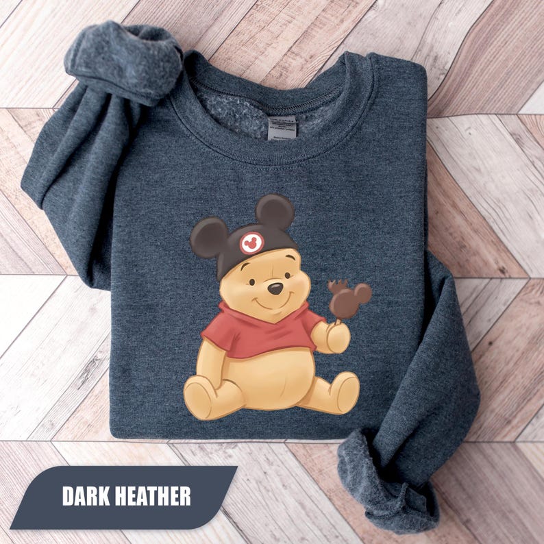 Pu&ograve; includere: Felpa color antracite scuro con un orsetto dei cartoni animati con un cappello di Topolino e un dolcetto al cioccolato. L'orso indossa una camicia rossa. Il testo "DARK HEATHER" &egrave; visualizzato nella parte inferiore dell'immagine.