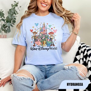 Puede incluir: Camiseta azul claro con un gr&aacute;fico colorido de personajes de Toy Story y un castillo, con el texto "Walt Disney World". El dise&ntilde;o incluye estrellas, corazones y globos. La camiseta es de un material suave.